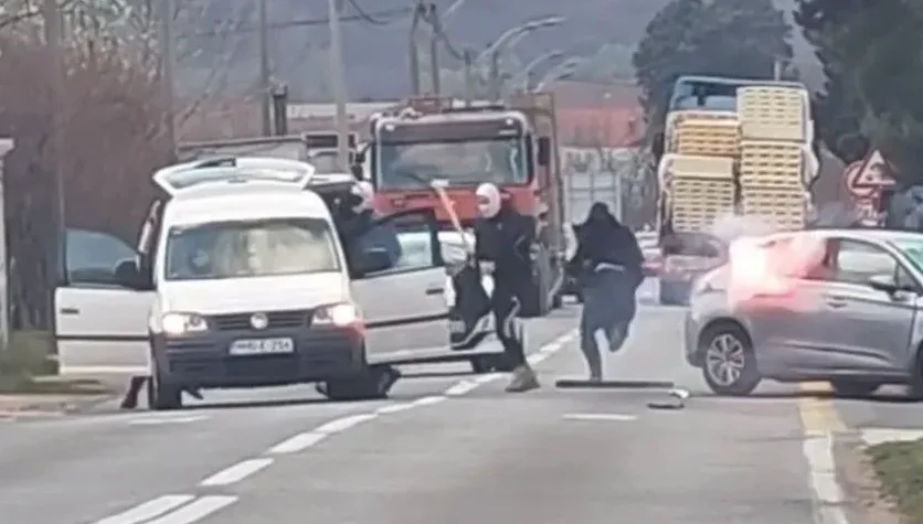 Dva lica sa fantomkama na glavi napadaju srebrni automobil na cesti, jedan drži motku, a drugi u rukama ima zapaljivi predmet. U pozadini se vide bijeli kombi, kamion i kamioni natovareni robom.