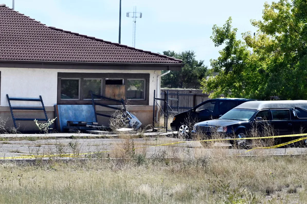 Crna limuzina i kombi parkirani ispred napuštene zgrade sa žutom trakom