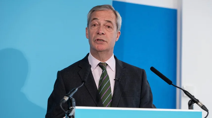 Nigel Farage, političar, govori za mikrofonom na plavoj pozadini.