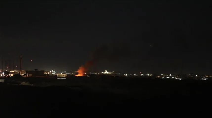 Goreći plamenovi i gusti crni dim koji se dižu u noćnom nebu iznad osvijetljenog grada.