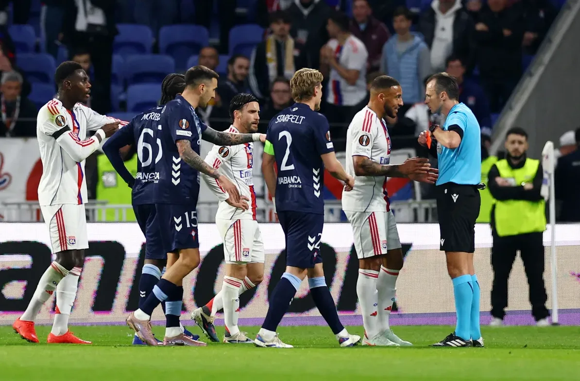 Fudbalski igrač u bijelom dresu u interakciji sa sudijom koji drži crveni karton.