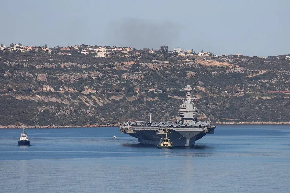 Američki nosač aviona plovi mirnim morem, uz obalu sa naseljem.