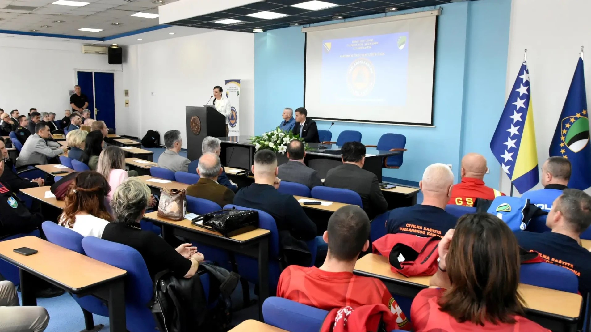 Amfiteatar sa predavačem za govornicom i publikom koja sjedi u klupama.