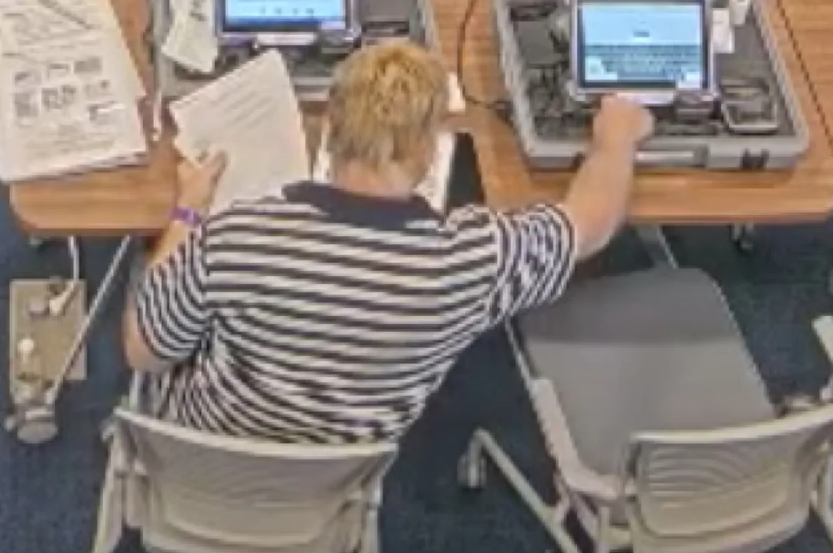 Osoba sjedi za stolom i radi na laptopu u tihoj sobi.