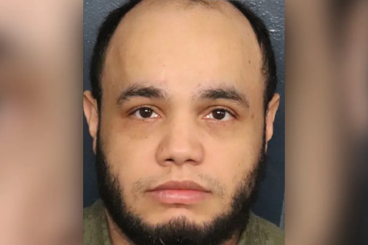 Portret muškarca s kratkom crnom kosom, obrijanih obrva, smeđim očima i urednom bradom, obučen u tamnu majicu.