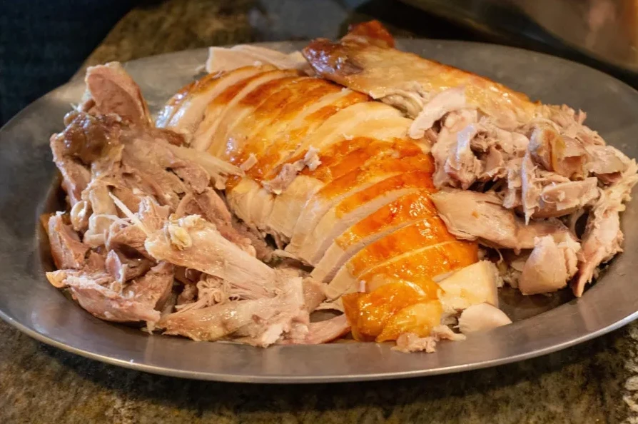 Odrezani komadi pečene piletine sa hrskavom kožom i rastrganim mesom od pečene piletine na metalnom tanjiru.