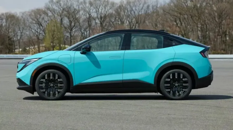 Plavi Nissan Ariya električni krosover parkiran na asfaltiranoj površini sa drvećem u pozadini.