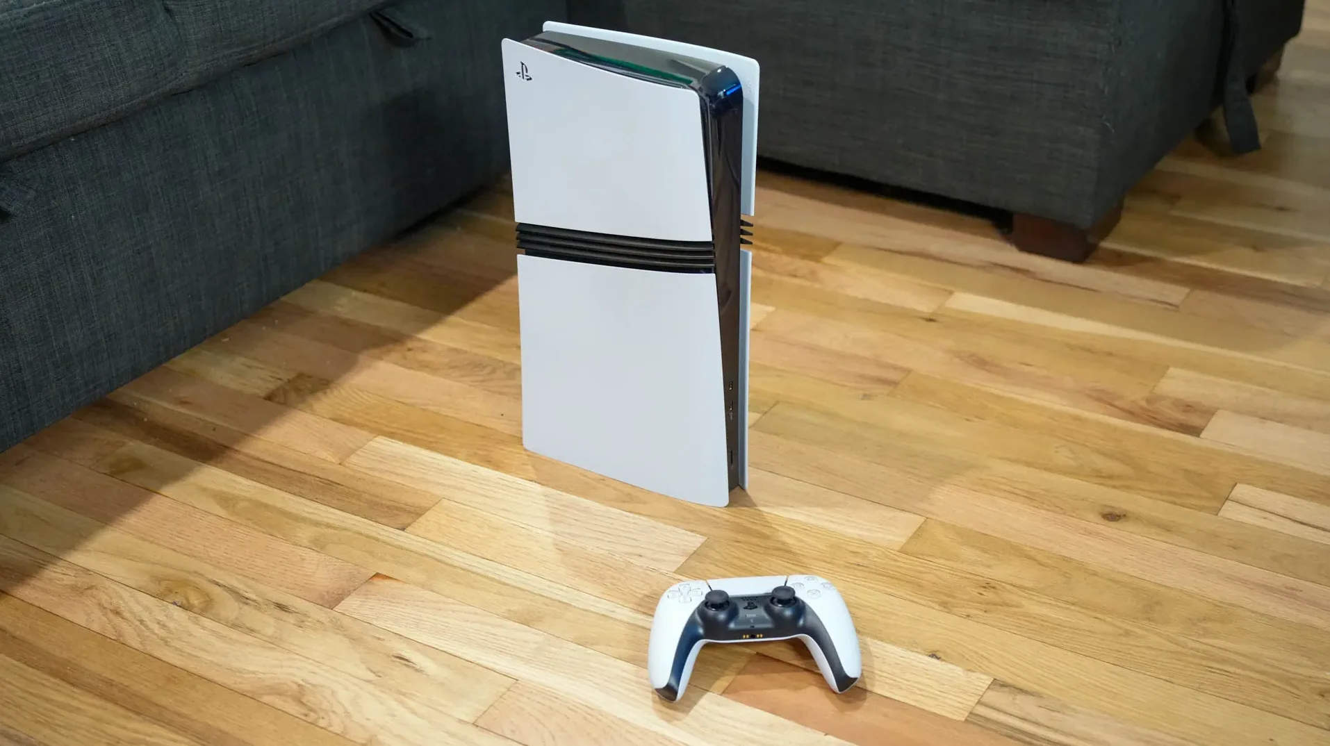 Konzola PlayStation 5 sa bežičnim džojstikom ispred nje na drvenom podu.