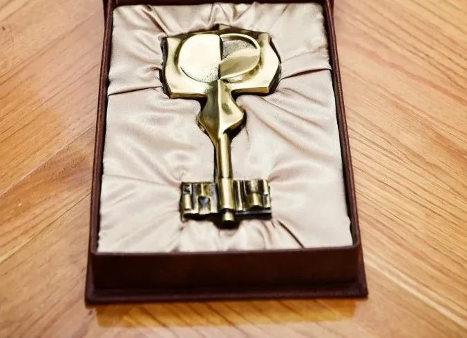 Bronzani ključ sa grbom ili amblemom na vrhu, smješten u tamnosmeđoj kutiji obloženoj svilenkastom tkaninom bež boje.
