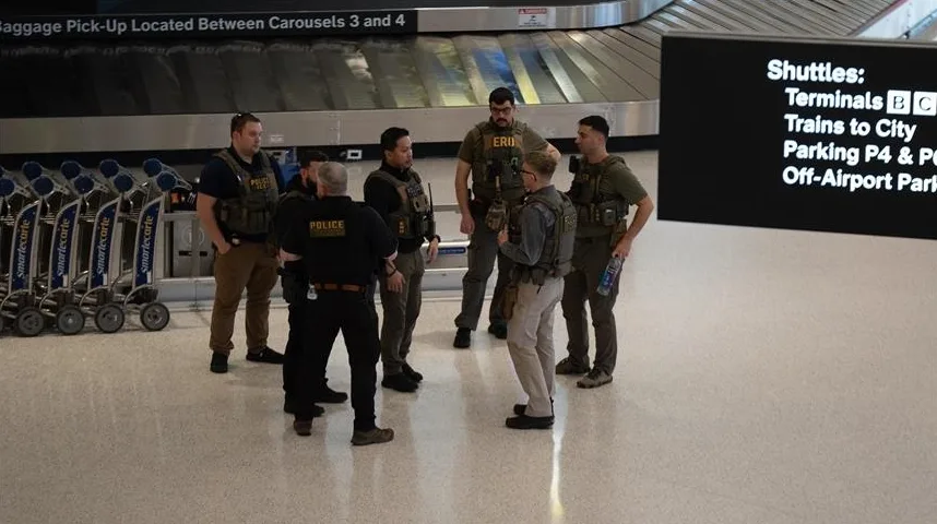 Grupa policajaca u uniformama i pancirima stoji na aerodromskom terminalu ispred pokretne trake za prtljag.