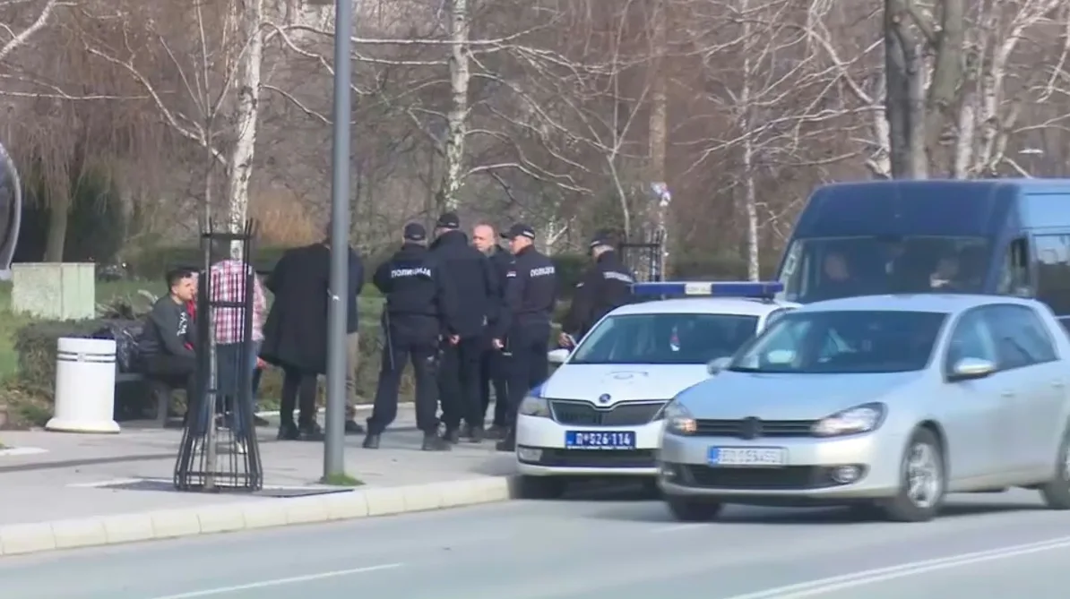 Policijski službenici u uniformama okupljeni pored policijskog vozila i kombija na ulici.