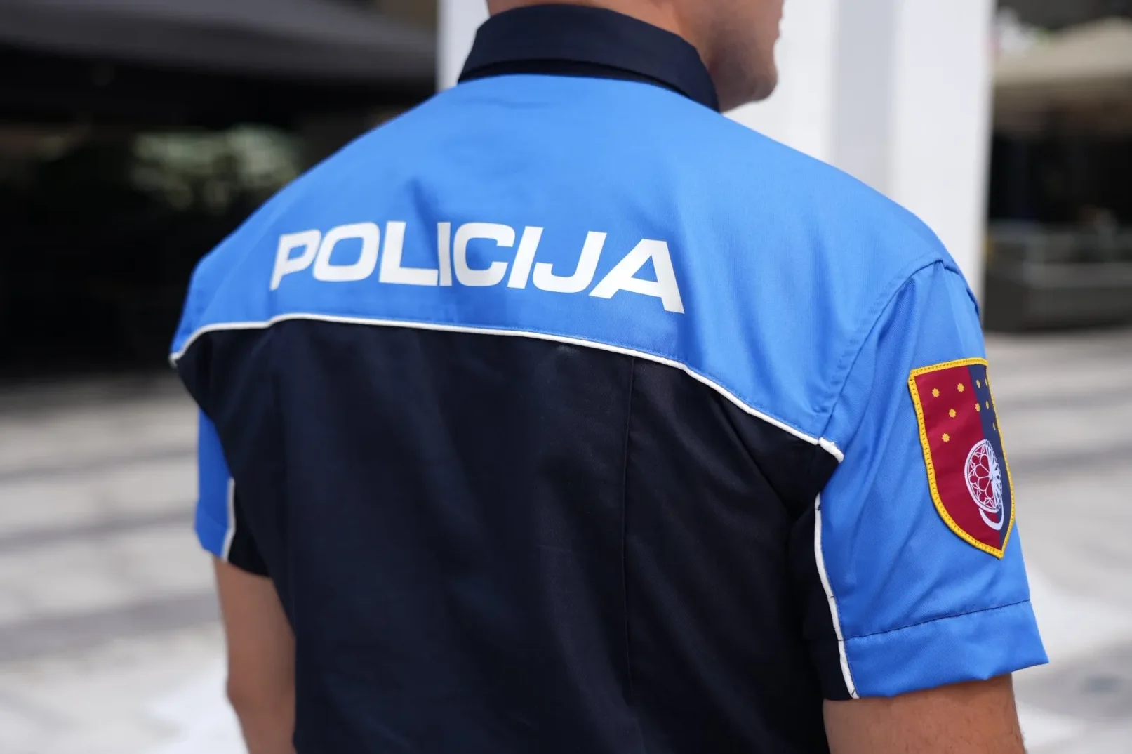 Policajac u plavoj uniformi sa natpisom 'POLICIJA' na leđima i grbom na rukavu.