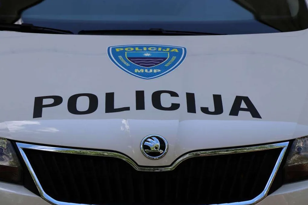 Detalj prednjeg dijela bijelog policijskog vozila sa natpisom 'POLICIJA' i grbom Ministarstva unutrašnjih poslova (MUP).