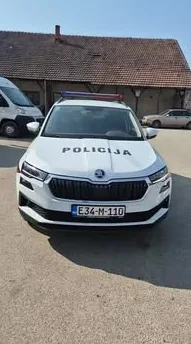 Prednji dio bijelog policijskog vozila marke Škoda Kodiaq sa upaljenom rotacijom i ispisom "POLICIJA" na haubi.