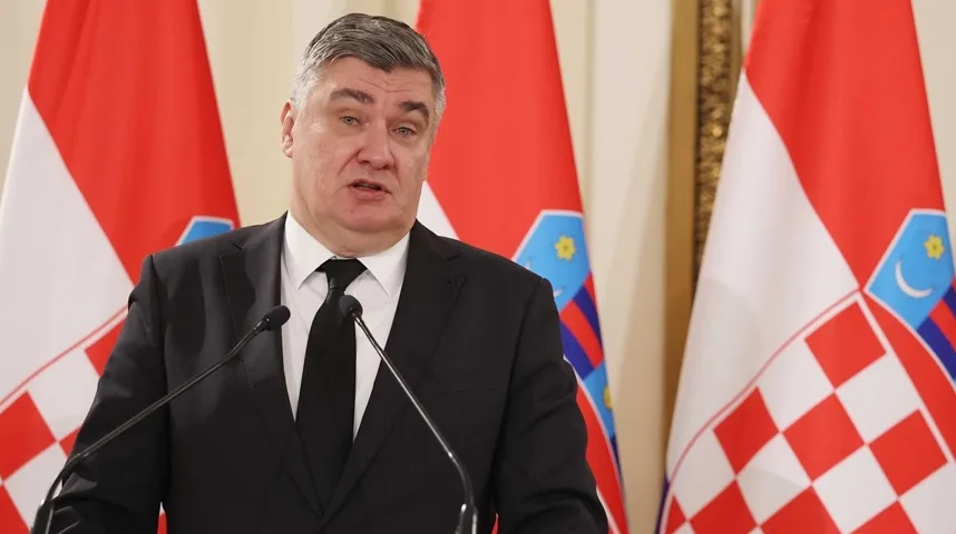 Čovjek u crnom odijelu i bijeloj košulji sa crnom kravatom stoji ispred dvije zastave Republike Hrvatske.