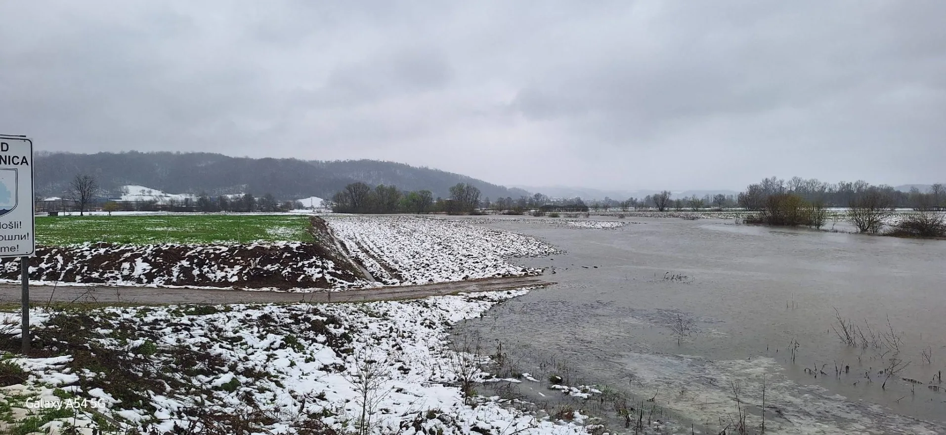 Poplavljeno polje sa snijegom pored puta u selu.