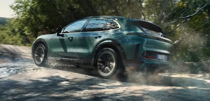 Tamnozeleni Porsche Cayenne koji vozi po makadamskom putu u šumi, podižući prašinu i prskajući vodu.