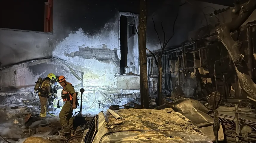 Dva vatrogasca u punoj opremi pregledaju uništenu zgradu i automobil nakon požara.