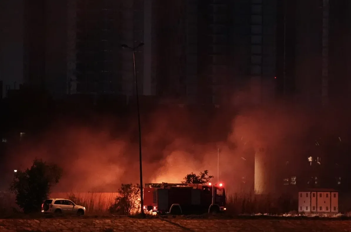 Vatrogasno vozilo sa upaljenim rotacijama na mjestu požara, okruženo gustim dimom u noćnim satima.