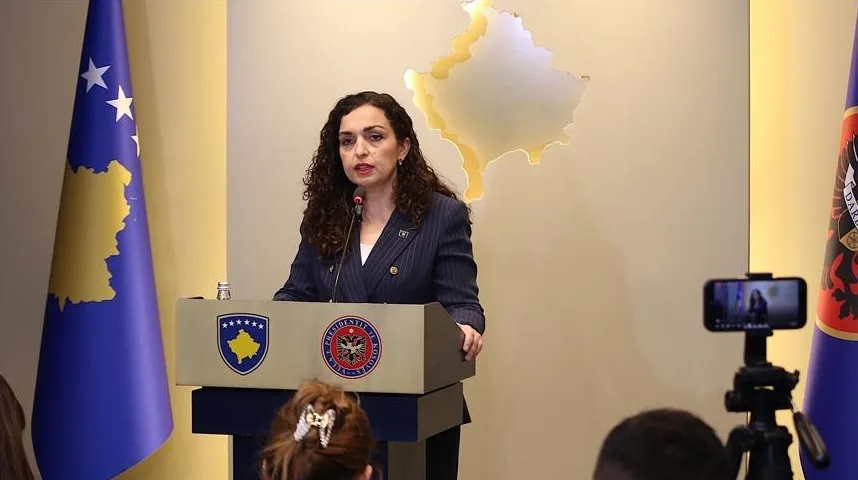 Predsjednica Kosova Vjosa Osmani govori za govornicom ispred zastava Kosova i s grbom Kosova na postolju.