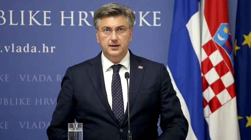 Premijer Republike Hrvatske, Andrej Plenković, u tamnom odijelu i sa tamnom kravatom sa bijelim tačkicama, stoji ispred mikrofona. U pozadini se vide zastave Republike Hrvatske i Evropske Unije.
