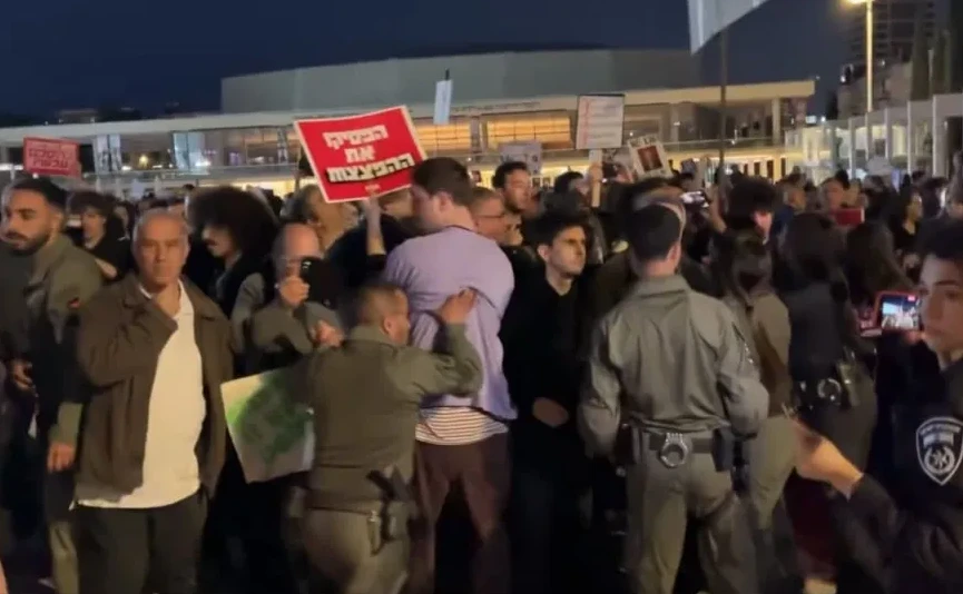 Grupa ljudi na protestu, neki nose natpise na hebrejskom, a policija ih nadgleda.