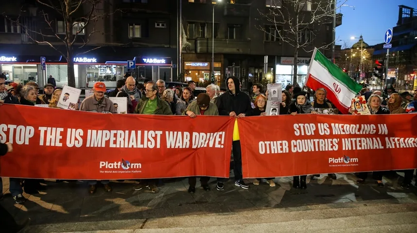 Grupa ljudi na ulici drži transparent na kojem piše "STOP THE US IMPERIALIST WAR DRIVE!" i "STOP US MEDDLING IN OTHER COUNTRIES' INTERNAL AFFAIRS", te iransku zastavu.