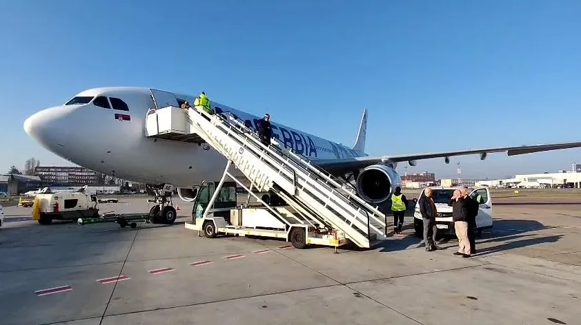 Putnici se ukrcavaju u avion Er Srbije koristeći pokretne stepenice na aerodromu