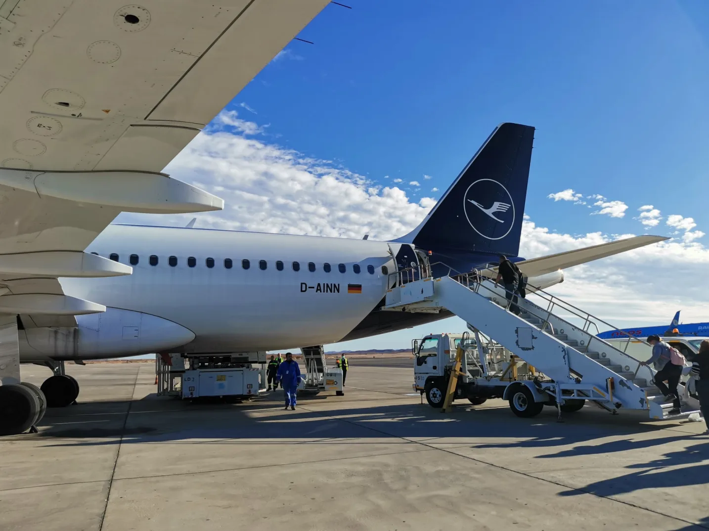 Putnik se ukrcava na avionsku letjelicu Lufthansa putem stepenica na aerodromu.