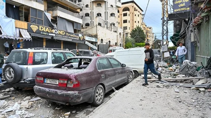 Dva dječaka hodaju kroz ruševine ulica prepunih olupina automobila i šuta. Jedan dječak je obučen u crnu majicu i plave farmerke, a drugi u bijelu majicu i plave farmerke. U pozadini su vidljivi oštećeni automobili, uključujući bordo sedan sa razbijenim prozorima i srebrni SUV.