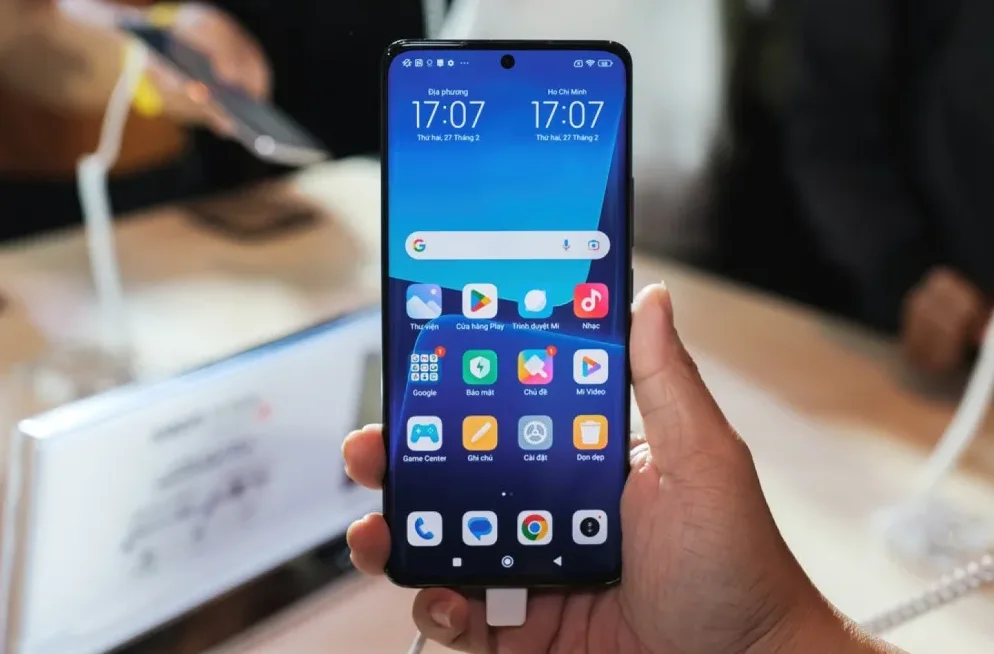 Ruka drži moderni mobilni telefon s prikazom početnog ekrana i ikonama aplikacija.