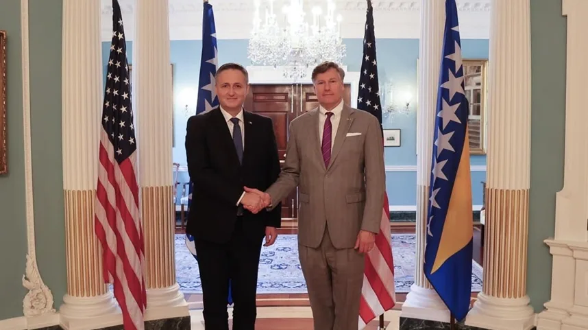 Dva muškarca rukuju se ispred zastave Sjedinjenih Američkih Država i zastave Bosne i Hercegovine.