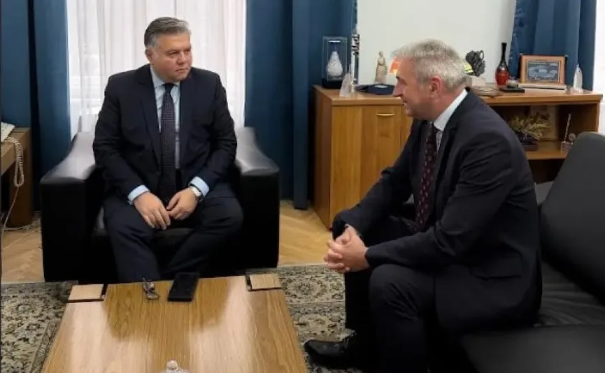 Dva muškarca u formalnim odijelima sjede u uredskom prostoru i razgovaraju.