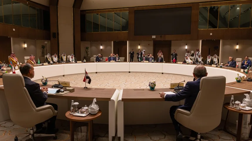 Grupa muškaraca u tradicionalnoj arapskoj odjeći i odijelima sjedi za velikim ovalnim stolom na sastanku.