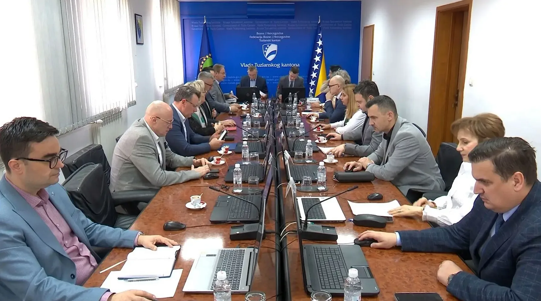 Grupa ljudi sjedi oko velikog drvenog stola na sastanku Vlade Tuzlanskog kantona.