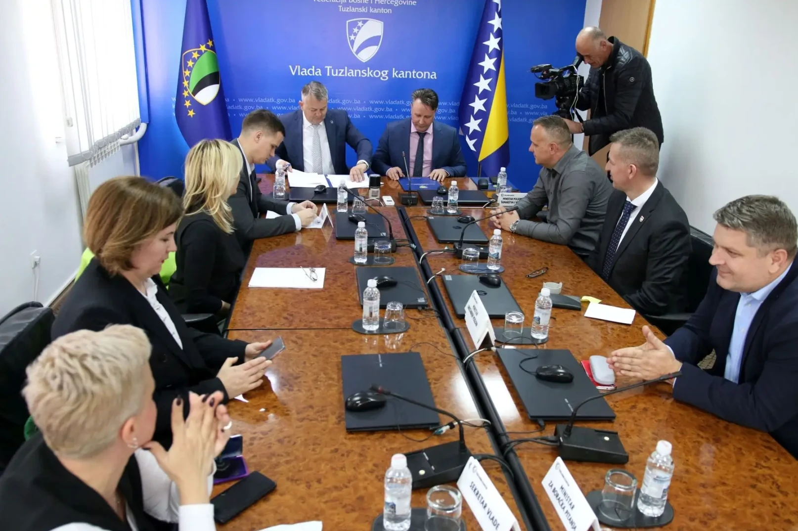 Članovi Vlade Tuzlanskog kantona sjede za stolom tokom sastanka, dok je jedan od učesnika sniman profesionalnom video kamerom.