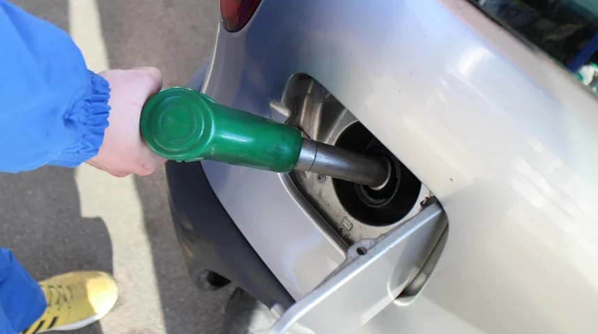 Ruka u plavoj jakni drži zelenu mlaznicu za gorivo koja se nalazi u rezervoaru automobila.