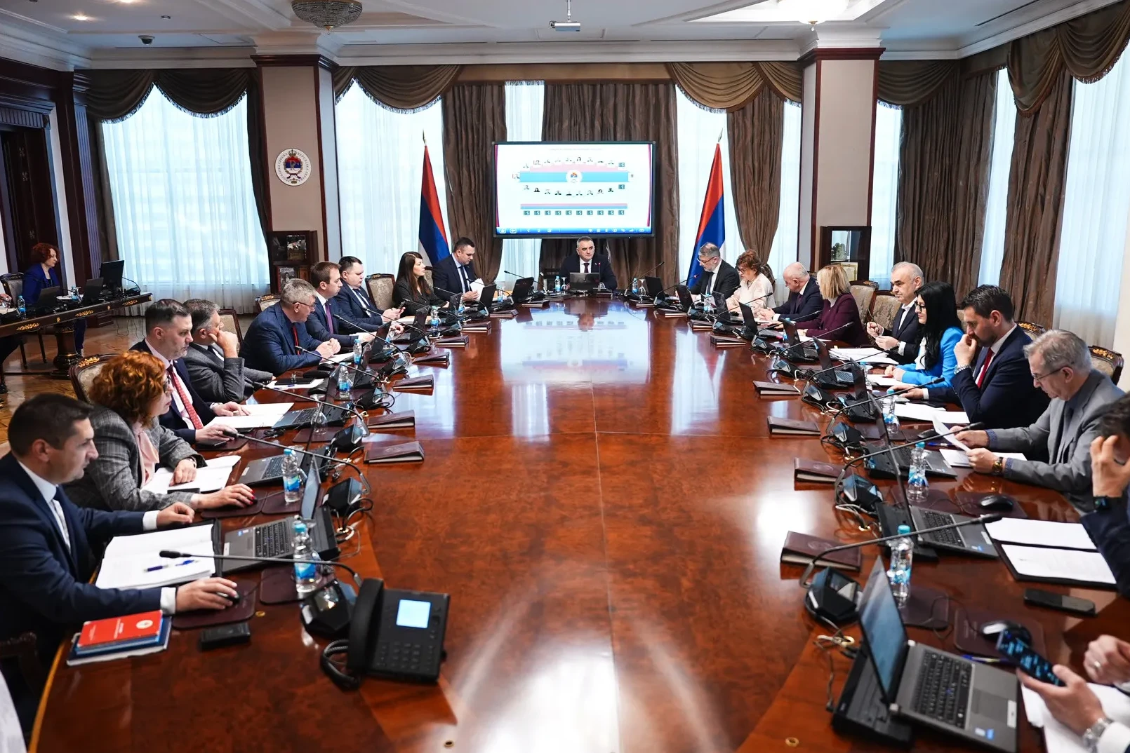 Sjednica zvaničnika za velikim drvenim stolom, ispred njih laptopi i dokumenti.