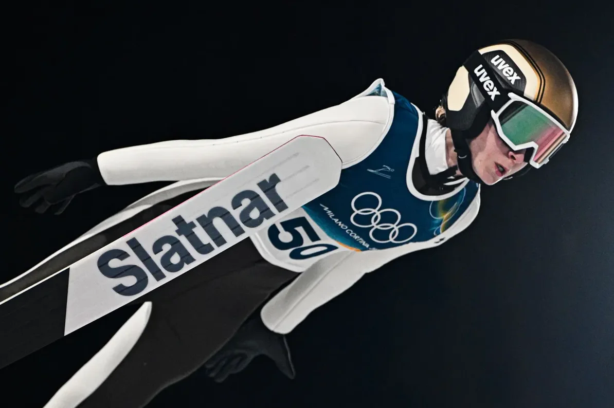 Skijaš u letu sa skijama na kojima piše Slatnar i broj 50, te olimpijski krugovi.