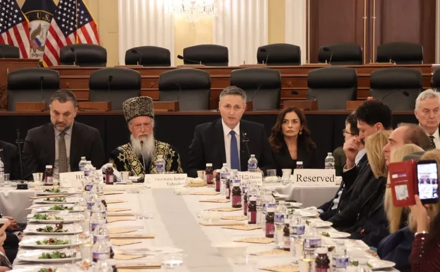 Grupa zvaničnika sjedi za stolom sa tri američke zastave u pozadini.