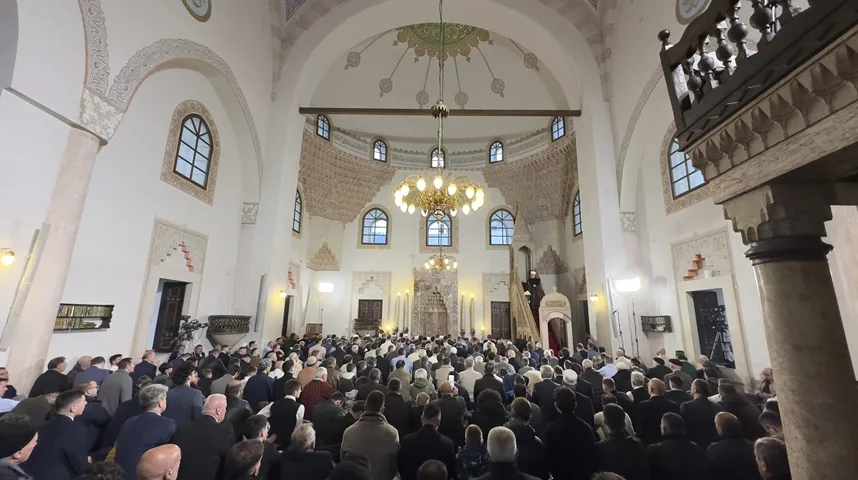 Skup vjernika u unutrašnjosti džamije, s naglaskom na vjerski objekat i prisutne ljude.