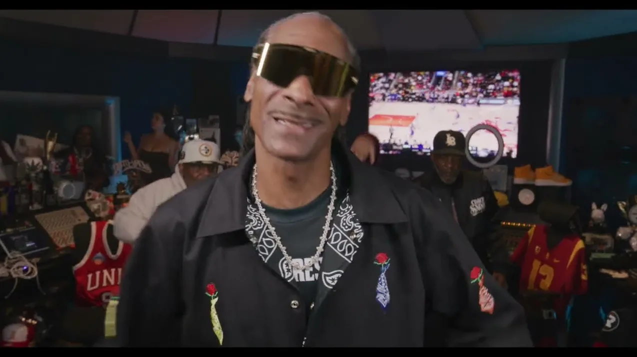 Snoop Dogg u crnom sakou sa paisley maramom i lančićem, nosi velike sunčane naočare.