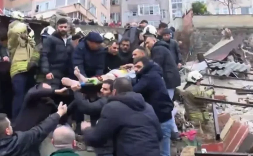 Grupa spasitelja, uključujući vatrogasce u zaštitnoj opremi, iznosi osobu na nosilima iz ruševina srušene zgrade.