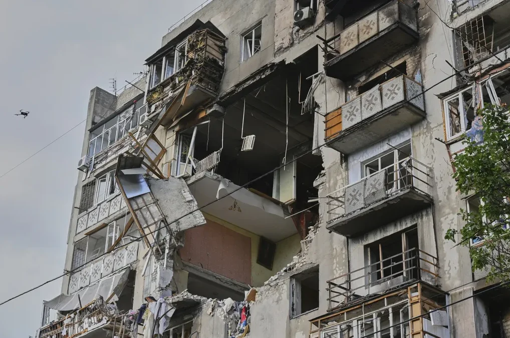 Uništena stambena zgrada s oštećenim balkonima i prozorskim otvorima, u daljini se vidi dron.