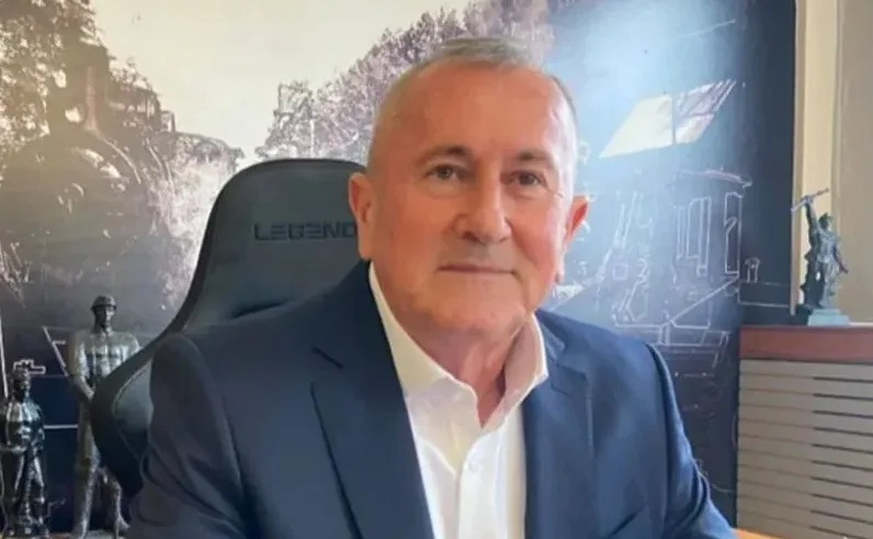 Portret starijeg muškarca u plavom odijelu i bijeloj košulji, sjedi u crnoj stolici s natpisom "LEGEND".