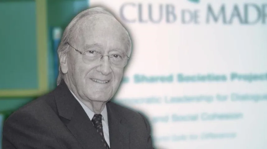 Portret starijeg gospodina sa naočalama, odjevenog u tamni sako i bijelu košulju s tamnom kravatom, sa logom "Club de Madrid" i natpisima o "Shared Societies Project" u pozadini.