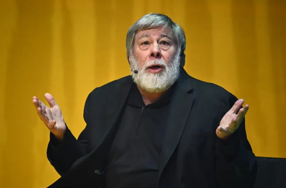 Steve Wozniak sa podignutim rukama ispred žute pozadine.