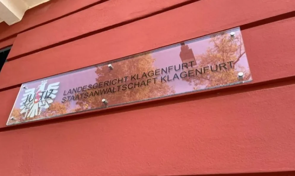 Natpis 'LANDESGERICHT KLAGENFURT STAATSANWALTSCHAFT KLAGENFURT' na staklenoj ploči ispred zgrade suda u Klagenfurtu.