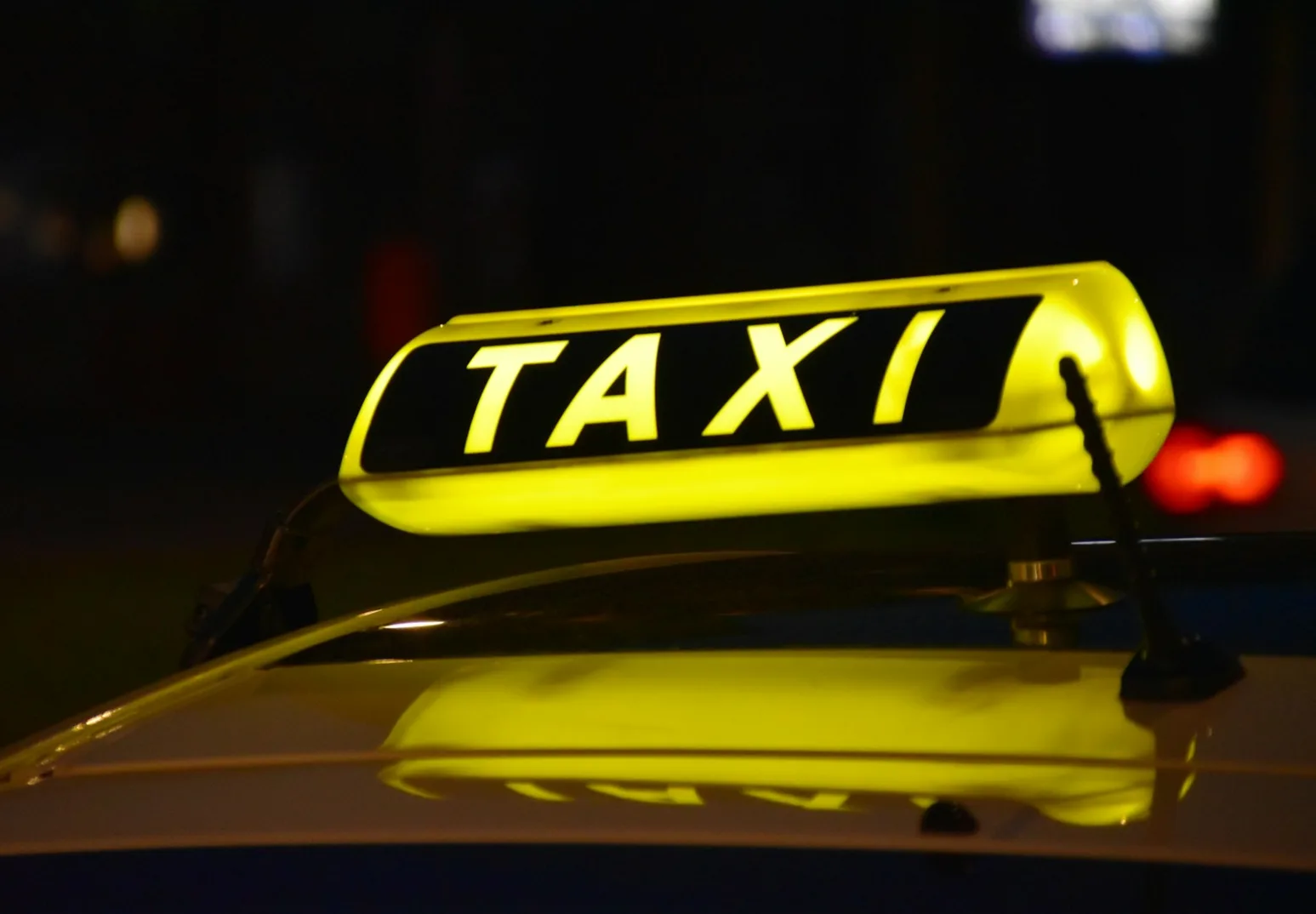 Osvijetljeni žuti "TAXI" znak na krovu automobila noću