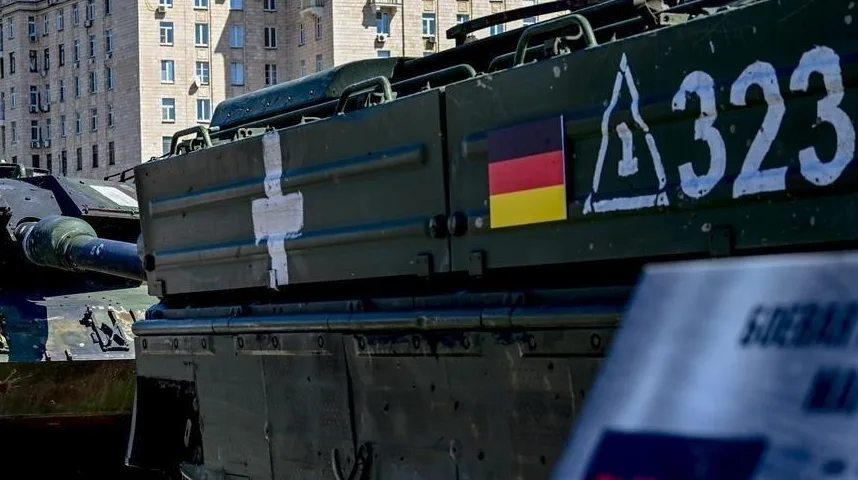 Tenk njemačke proizvodnje, vjerojatno Leopard 2, s istaknutom njemačkom zastavom i oznakom 'A323' na boku. Također se vidi bijela oznaka na boku tenka i natpis na ruskom jeziku na prednjem planu.